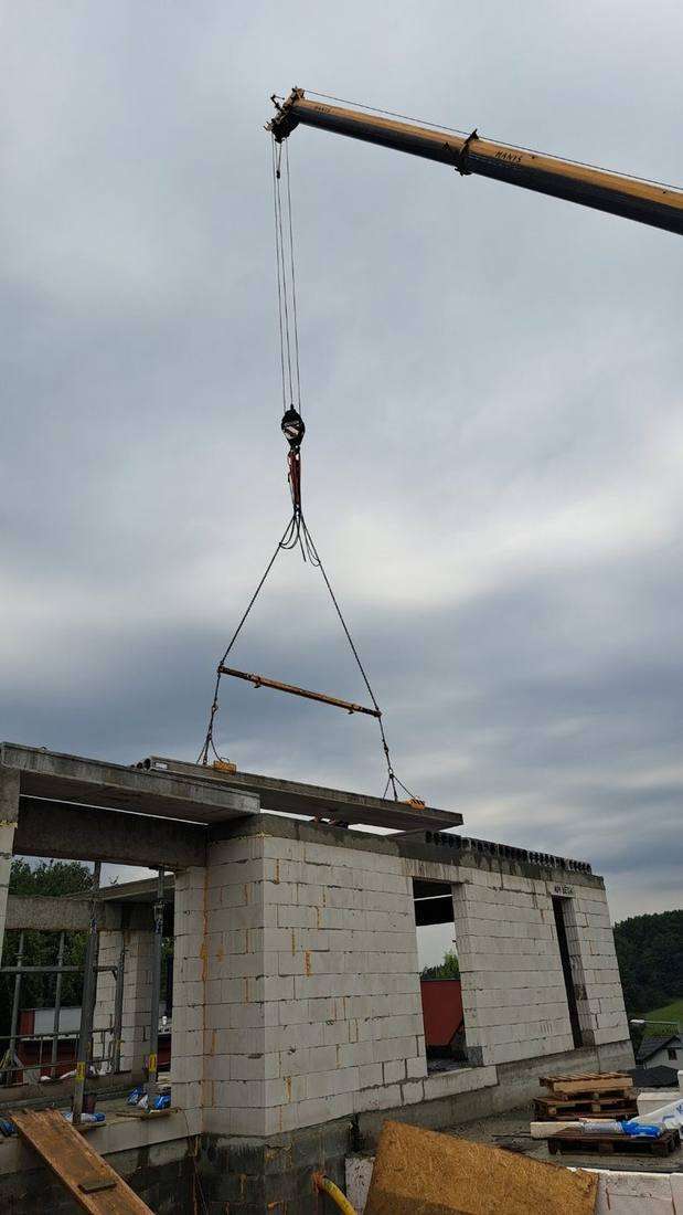 Jeřáb spouští betonový panel na zdivo Ytong – pracovníci asistují při uložení stropní desky na hrubou stavbu