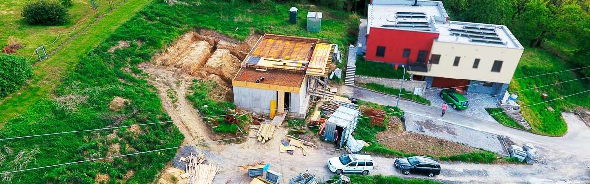 Panoramatický pohled na rozestavěný rodinný dům – hrubá stavba s viditelnou konstrukcí zdiva, stropními panely a připraveným krovem, okolní příroda Plzeňského kraje